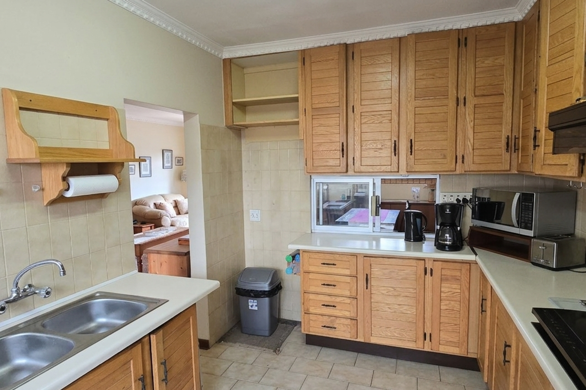 A functional kitchen featuring wooden cabinetry, a double basin sink, tiled backsplash, and integrated cooktop, offering a classic layout with direct access to the living area.