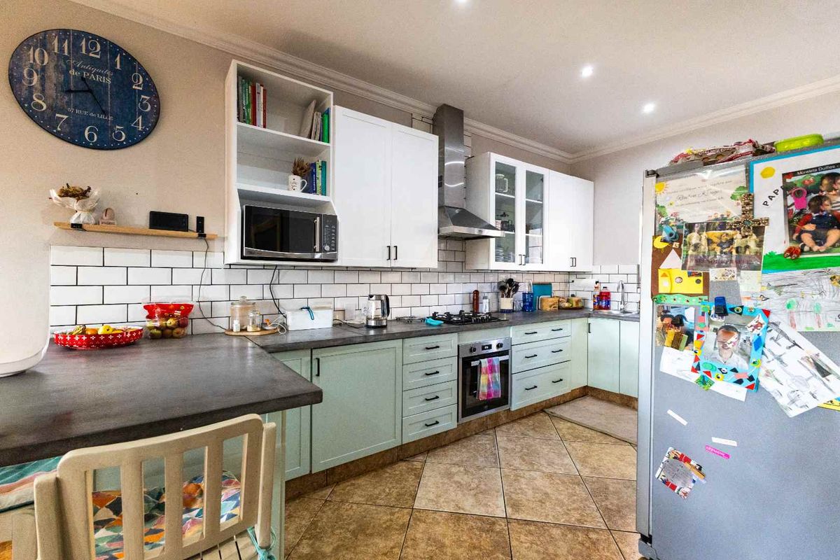 A functional kitchen featuring light green cabinetry, subway tile backsplash, dark countertops, and integrated stainless steel appliances including an oven and extractor fan.