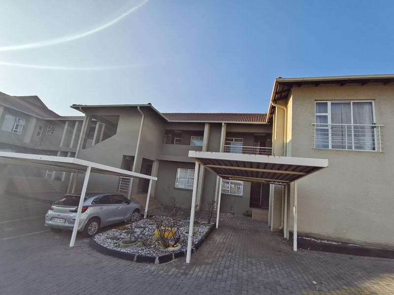 Front elevation of an apartment complex featuring covered parking bays, paved driveway, and balcony access.