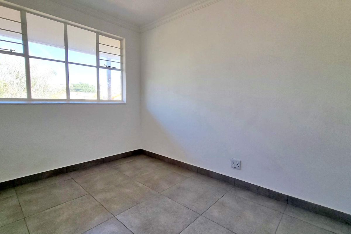 A bright, empty bedroom featuring neutral tiled flooring, clean white walls, and a large window providing natural light.