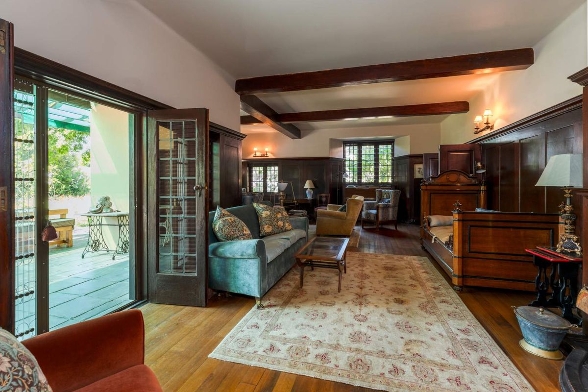 Spacious living area featuring rich timber wall paneling, exposed ceiling beams, hardwood flooring, and French doors opening onto an outdoor patio.