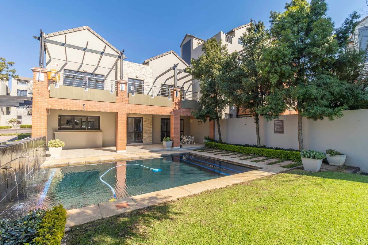 A well-maintained rear exterior view featuring a private swimming pool, a paved patio area, and a landscaped garden with mature trees.