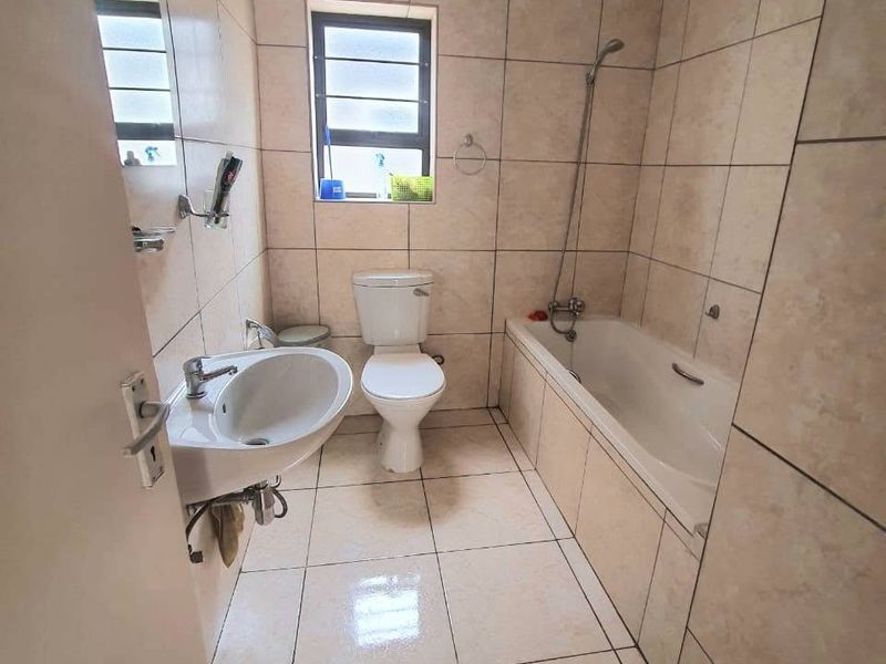 A functional bathroom featuring full-height ceramic wall tiling, a standard bathtub with shower mixer, pedestal basin, and toilet.