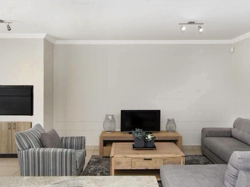 A well-maintained living room featuring a built-in fireplace, custom cabinetry, crown molding, and modern track lighting.