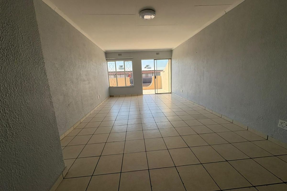 An empty, open-plan living area featuring tiled flooring, a sliding glass door leading to an outdoor space, and security bars on the windows.