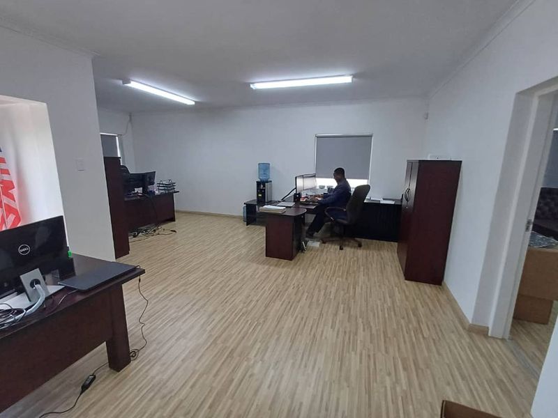 A functional office space featuring laminate flooring, bright overhead fluorescent lighting, and roller blinds, providing a practical environment for business operations.