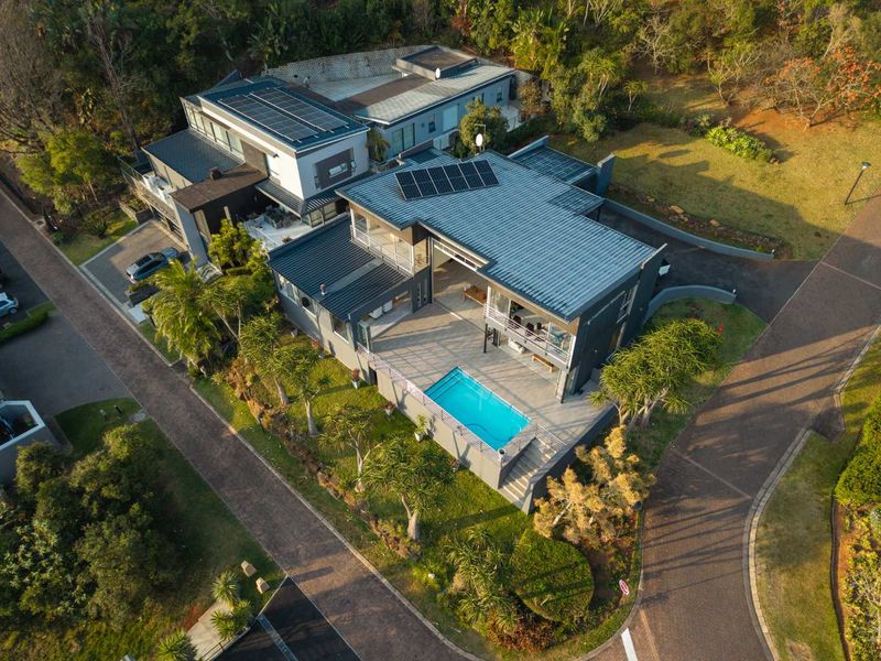 Aerial view of a modern multi-level residence featuring a swimming pool, solar panels, and landscaped grounds within a residential estate.
