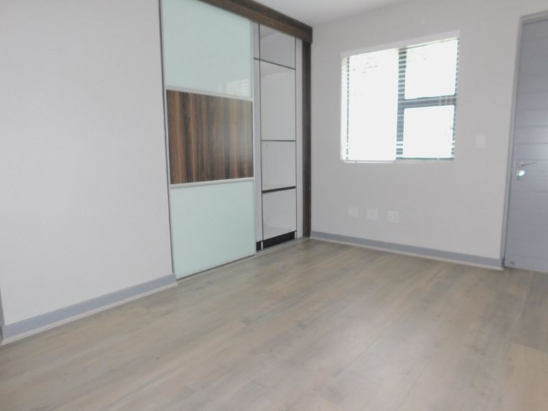 A bright, empty bedroom featuring modern laminate flooring, neutral walls, and contemporary built-in cupboards with sliding doors.