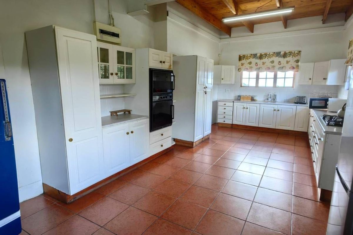Spacious farmhouse kitchen featuring white cabinetry, built-in oven, tiled flooring, and exposed timber ceiling beams.