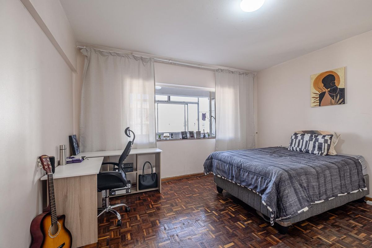 A well-lit bedroom featuring classic parquet flooring and a large window, providing a comfortable and functional living space.