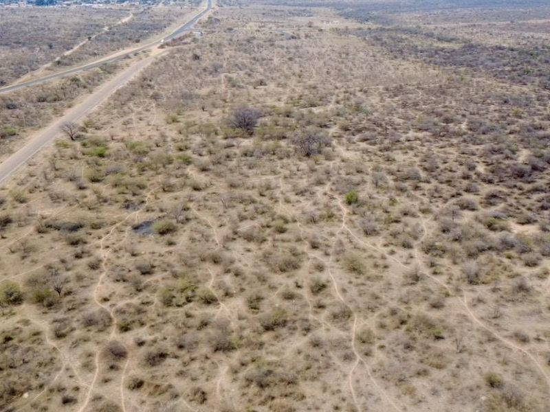 An aerial view of a large, undeveloped tract of land adjacent to a main road, featuring natural scrub vegetation and open terrain.