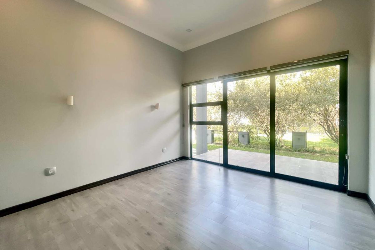 A bright, modern bedroom featuring light wood-look flooring, neutral walls, and large sliding glass doors that open to a private garden area.
