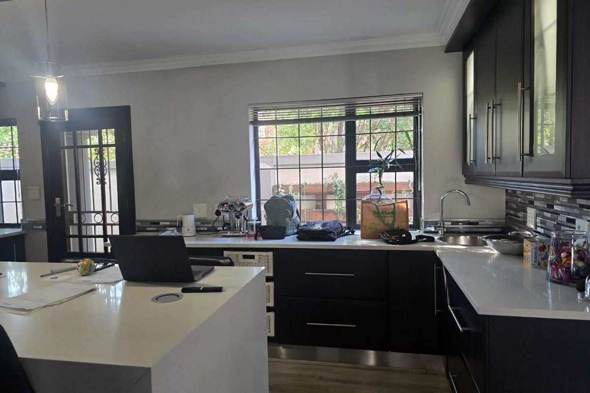 Modern kitchen featuring dark cabinetry, white stone countertops, a central island, and a tiled backsplash with a window overlooking the exterior.