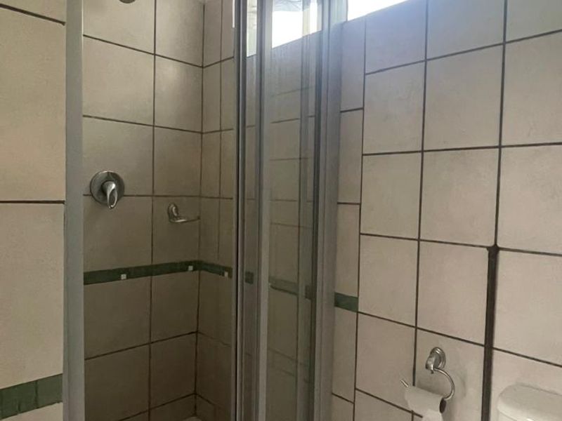 A functional bathroom featuring a shower enclosure with tiled walls and a standard toilet, requiring some cosmetic updates to the tiling and finishes.
