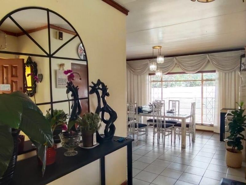 A bright dining area featuring tiled flooring and a large window with decorative curtains, providing a clear view of the outdoor space.