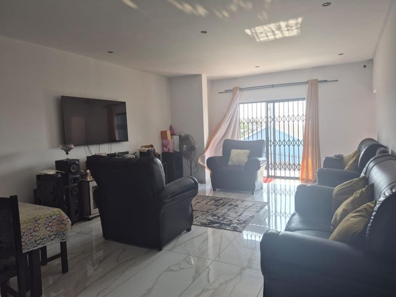 Spacious living room featuring modern white marble-look porcelain floor tiles, recessed downlighting, and a sliding glass door with security gate access to the exterior.