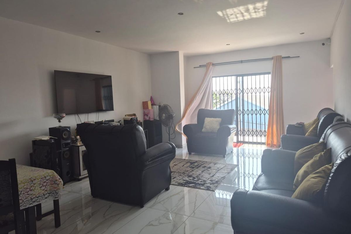 Spacious living room featuring modern white marble-look porcelain floor tiles, recessed downlighting, and a sliding glass door with security gate access to the exterior.