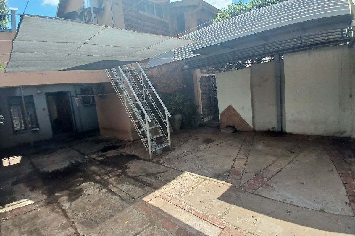 Rear courtyard area featuring a metal staircase, shade sail, and paved flooring, providing functional outdoor space with potential for improvement.