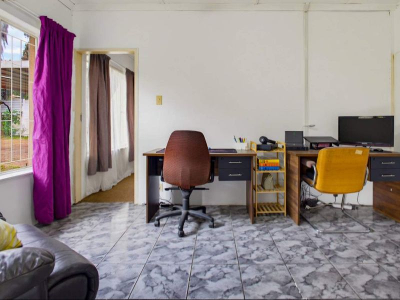 A functional office space featuring tiled flooring and a window with security bars, providing a practical area for work or study.