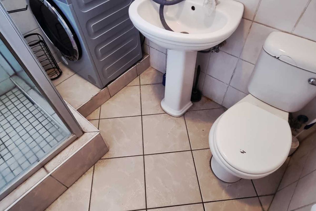 Compact bathroom featuring a shower enclosure, pedestal basin, and toilet, with integrated laundry plumbing connections.