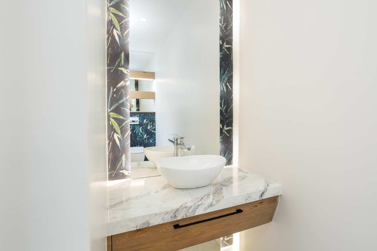 Modern bathroom featuring a floating vanity with marble countertop, vessel sink, and stylish backlit mirror with decorative side panels.