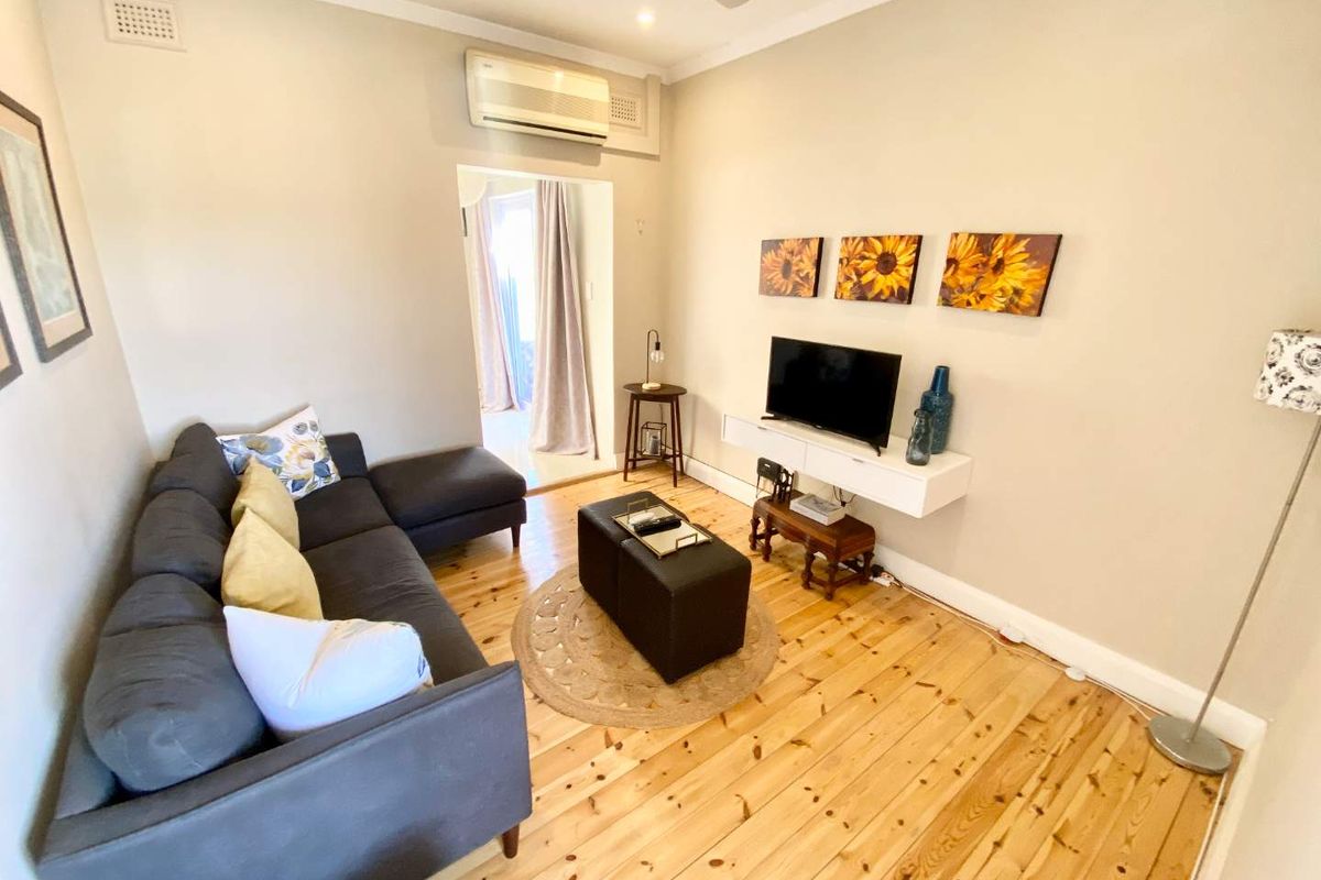A cozy living room featuring polished timber flooring, a wall-mounted air conditioning unit, and a ceiling fan.