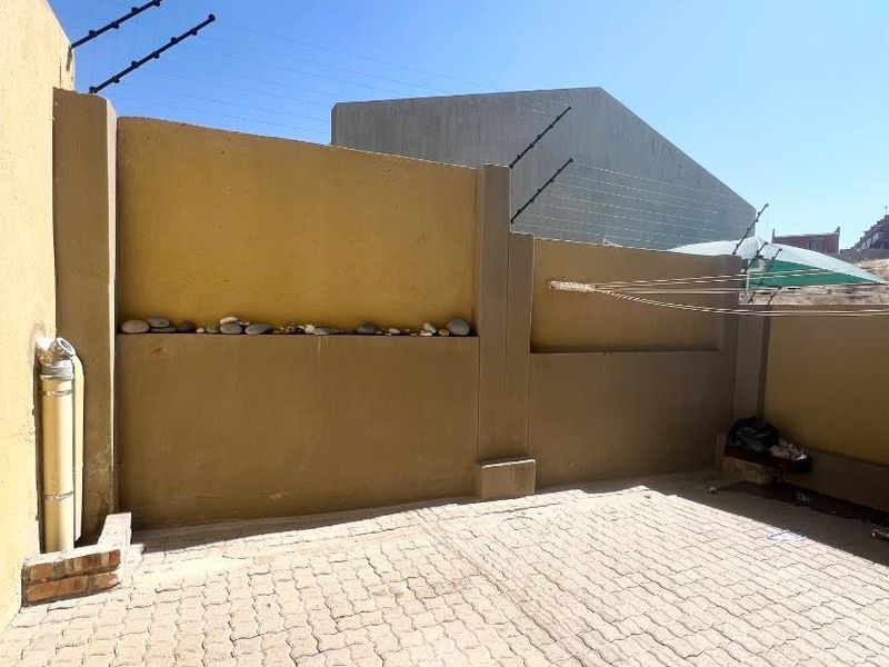 A paved rear courtyard area featuring high boundary walls with electric fencing and an external plumbing fixture.