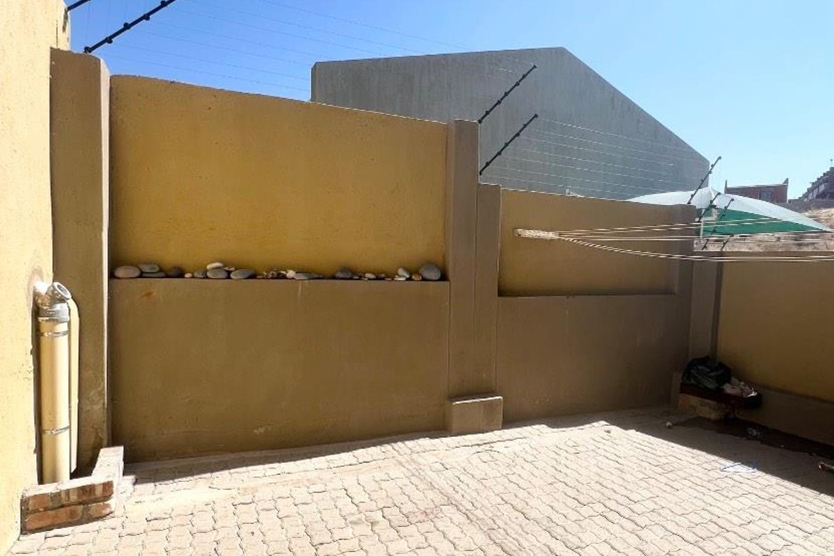 A paved rear courtyard area featuring high boundary walls with electric fencing and an external plumbing fixture.