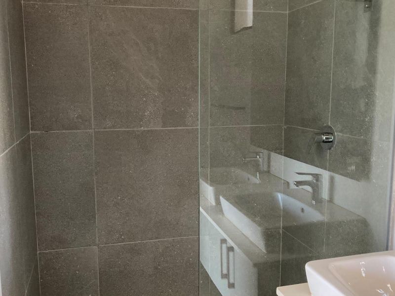 A modern bathroom featuring a glass-enclosed shower with grey tiled walls and a sleek vanity unit with a basin.