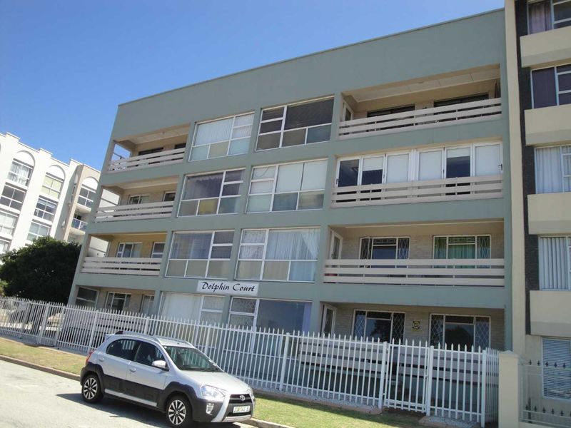 Front elevation of Dolphin Court apartment building featuring multi-level balconies, sliding glass doors, and perimeter security fencing.