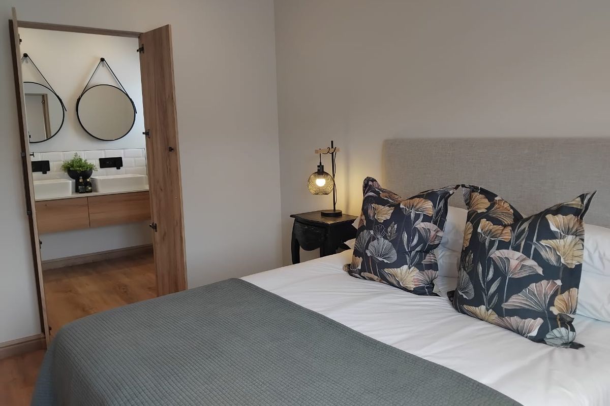 A well-maintained bedroom featuring a neutral color palette and an adjoining en-suite bathroom with modern vanity and double mirrors.