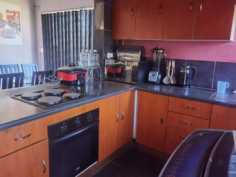 A functional kitchen featuring wood-tone cabinetry, dark laminate countertops, a built-in oven, and an electric hob, offering a practical layout for daily meal preparation.