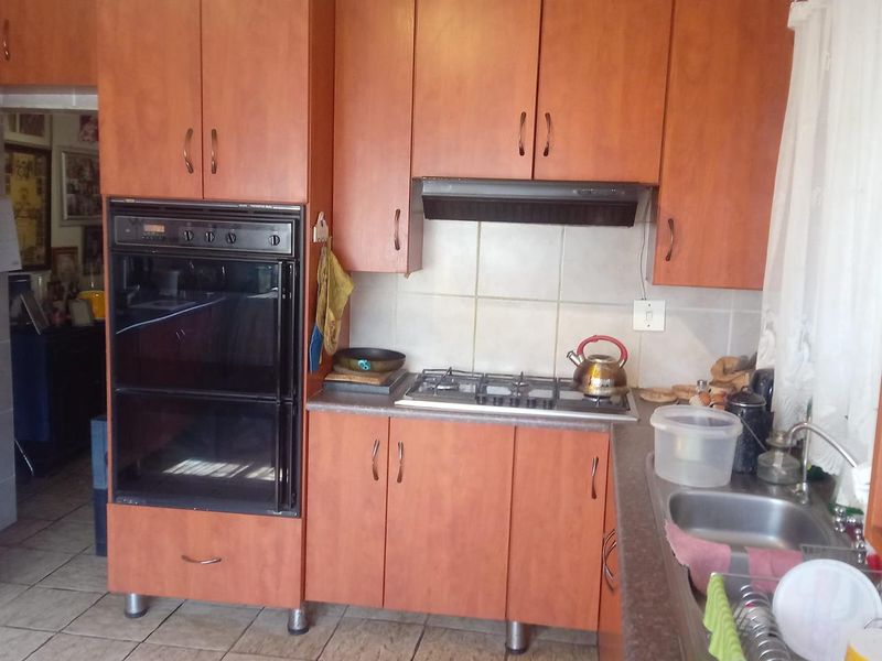 A functional kitchen featuring wood-look cabinetry, a built-in oven, gas hob with extractor, and tiled flooring with a double sink.