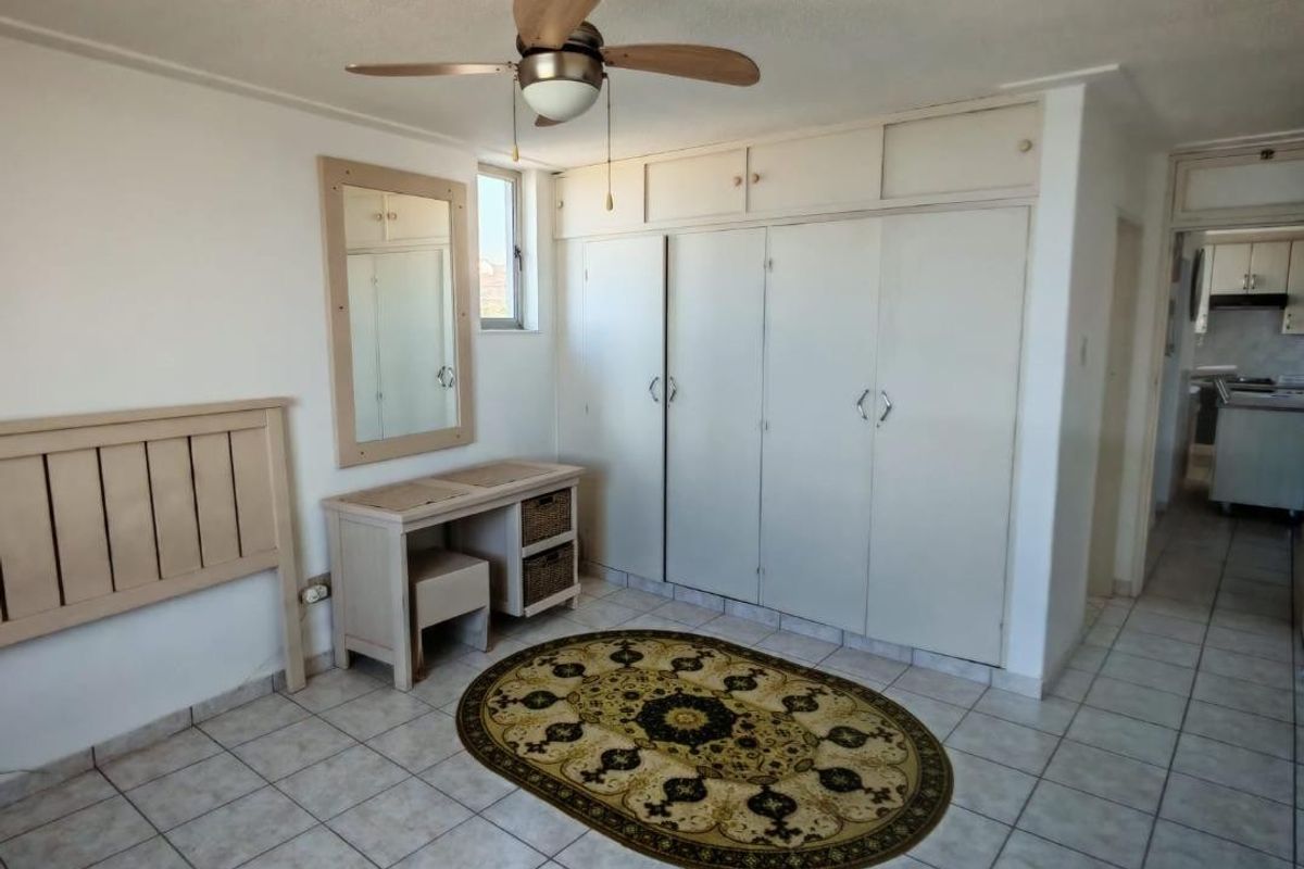 Bedroom featuring built-in cupboards with overhead storage, a ceiling fan, and tiled flooring, with a view into the adjacent kitchen area.