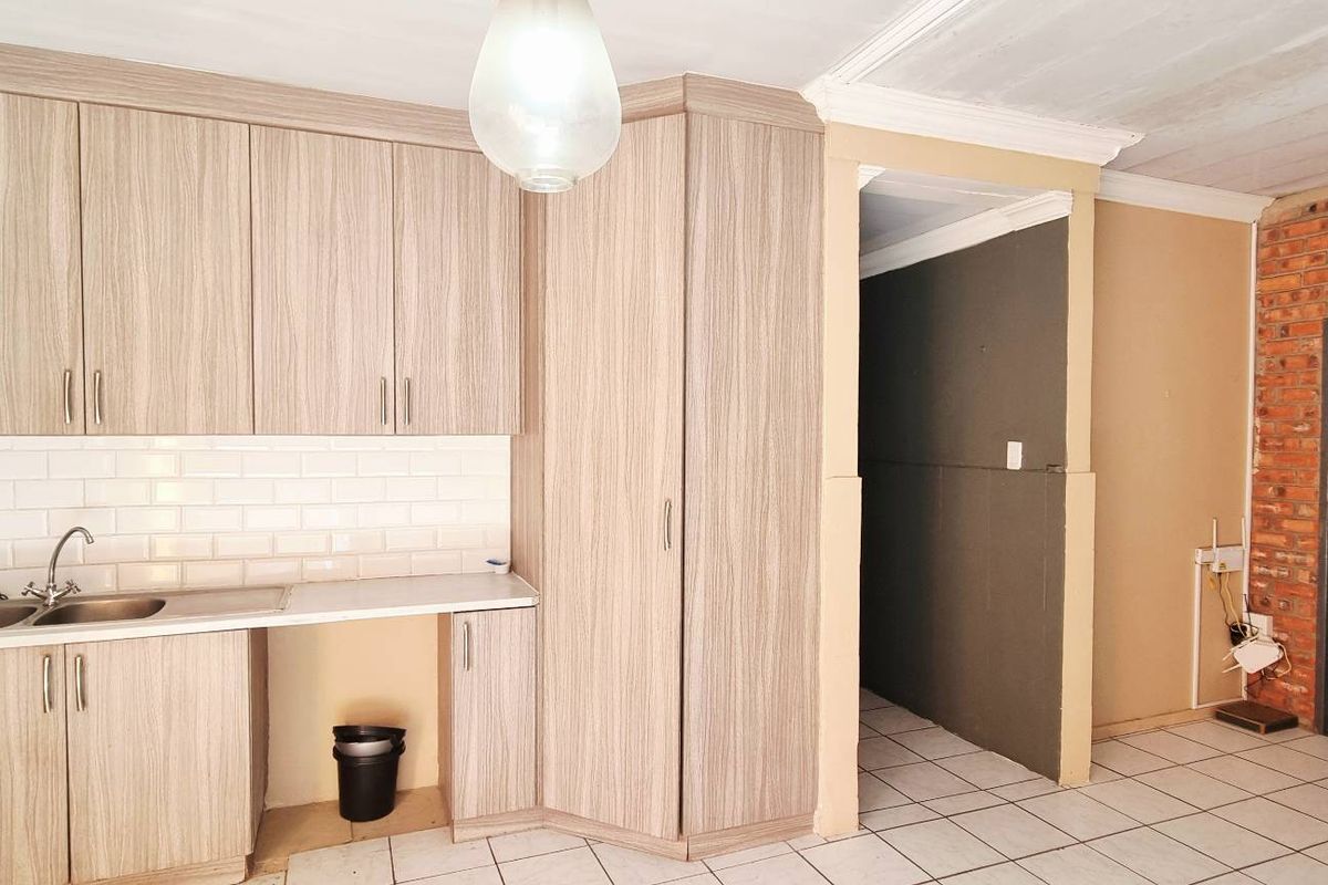 A compact kitchen featuring light wood-grain cabinetry, a subway tile backsplash, and a double sink, adjacent to an exposed brick wall and tiled flooring.