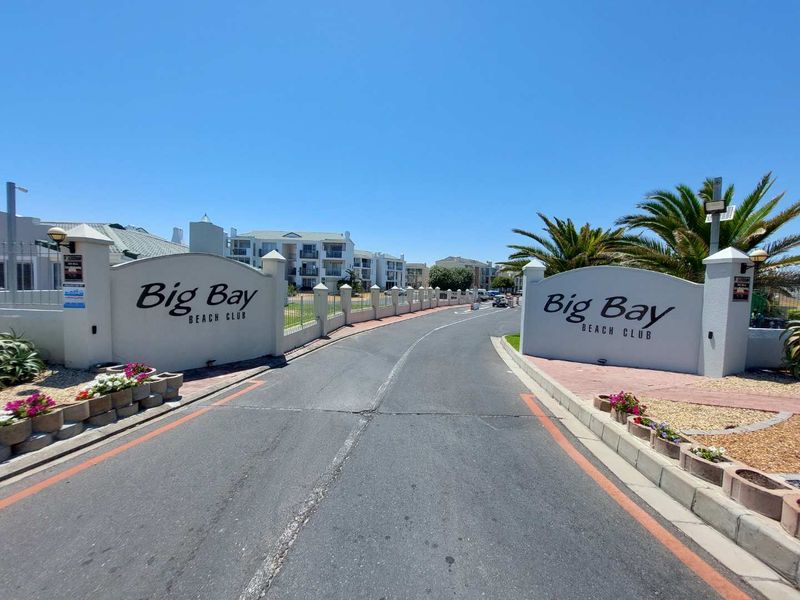 The entrance to Big Bay Beach Club, featuring a gated access point, paved driveway, and well-maintained perimeter walls and landscaping.