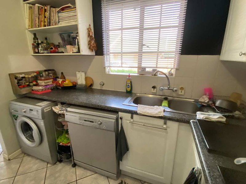 Functional kitchen area featuring a double bowl stainless steel sink, laminate countertops, built-in cabinetry, and tiled flooring with a window for natural light.
