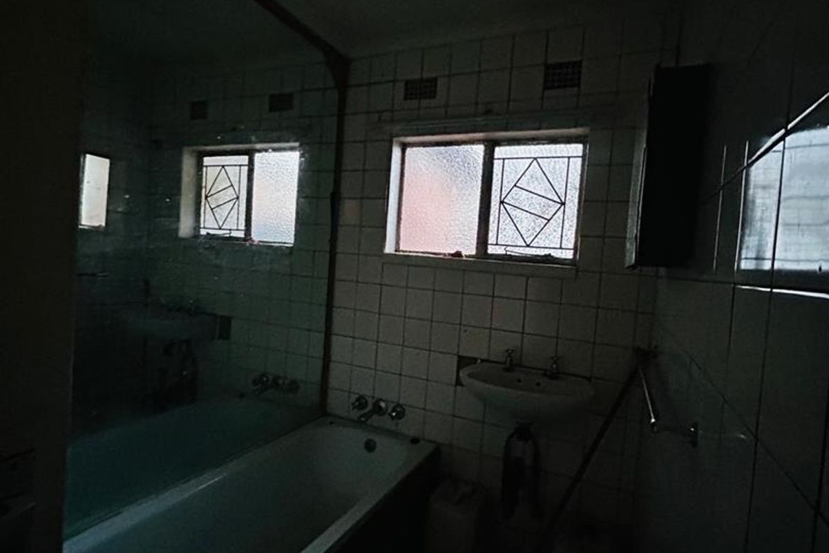 A dated bathroom featuring a bathtub, wall-mounted basin, and tiled walls. The space requires significant lighting improvements and modernization of finishes.