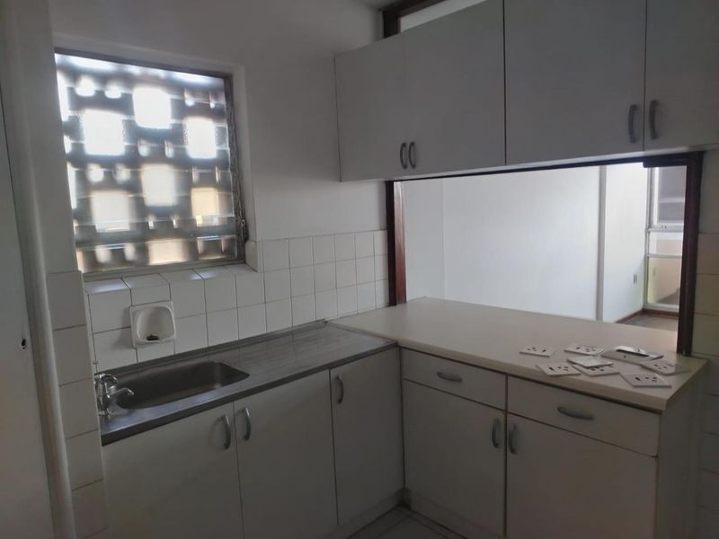 A functional kitchen featuring built-in cabinetry, laminate countertops, a stainless steel sink, and a tiled backsplash with a window for natural light.