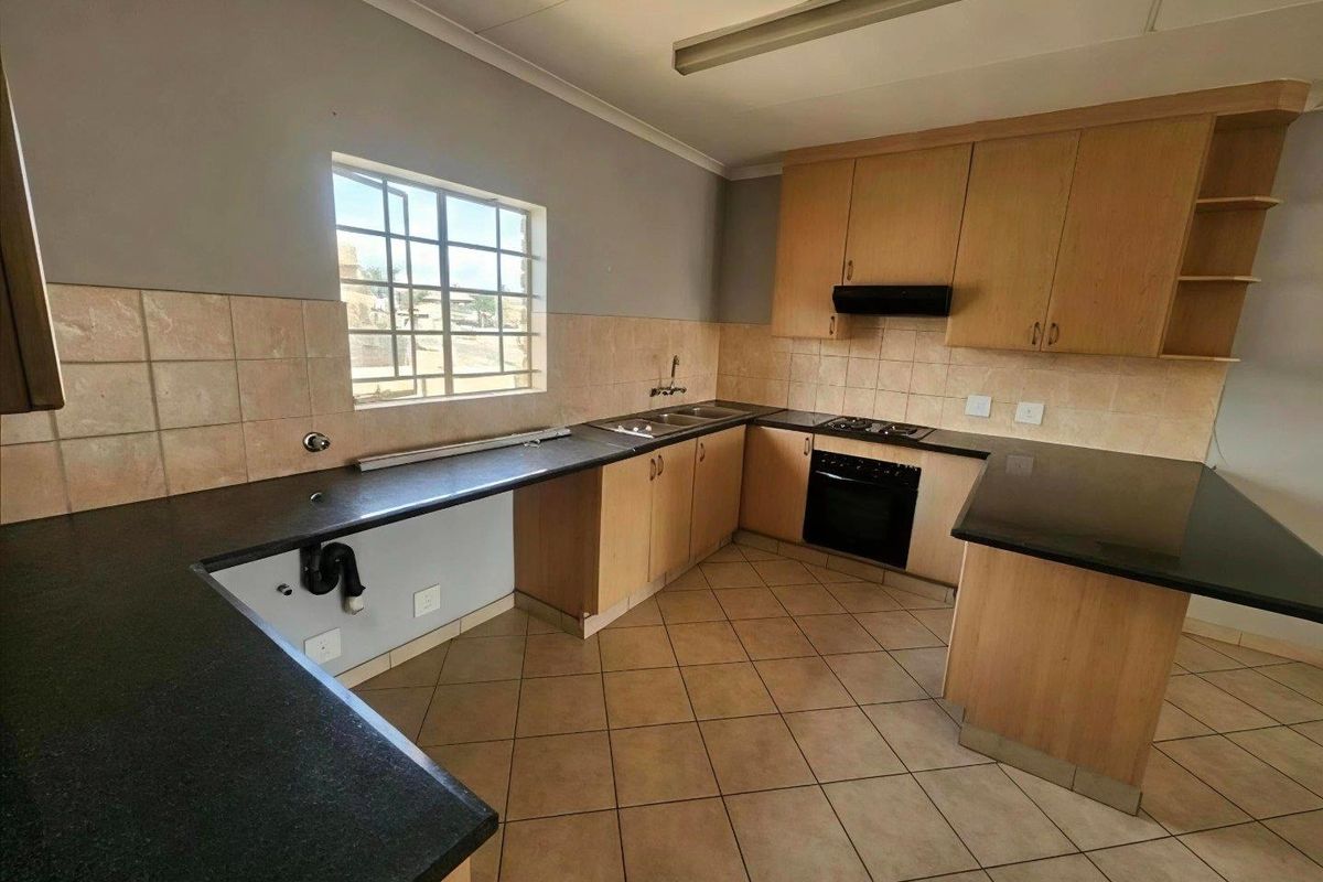 A functional kitchen featuring light wood cabinetry, dark countertops, built-in oven and hob, and tiled flooring. The space is vacant and ready for updates.