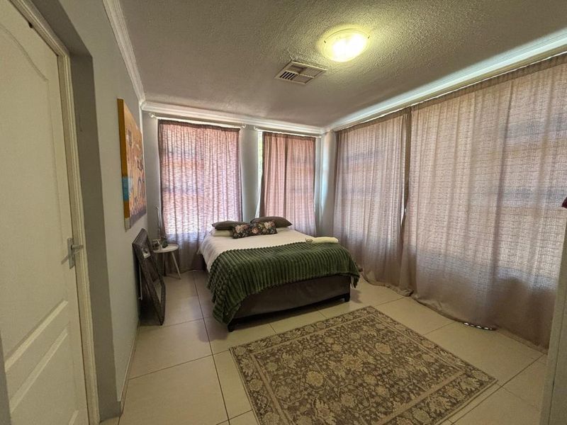 A bedroom featuring tiled flooring, cornice detailing, and ducted air conditioning, with large windows covered by floor-to-ceiling curtains.