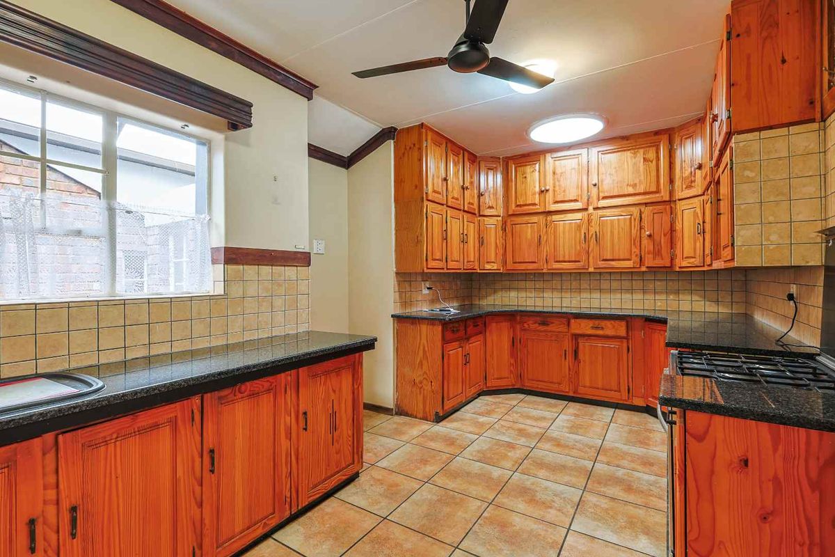 A functional kitchen featuring extensive wooden cabinetry, dark granite countertops, tiled splashbacks, and a built-in gas hob.