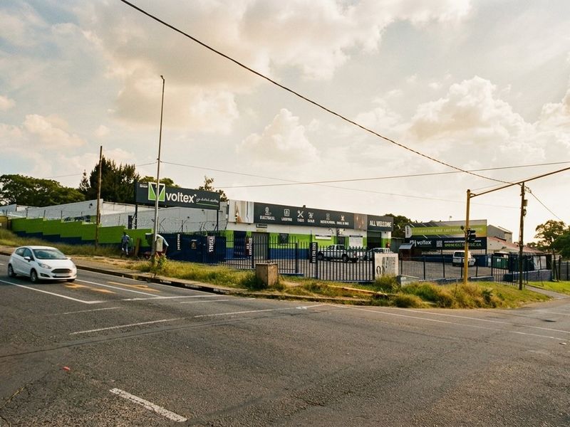 Street-level view of a commercial property featuring a fenced perimeter, paved driveway, and prominent signage along the main road.