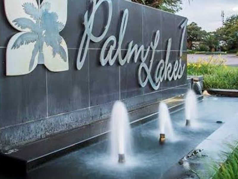 The entrance to Palm Lakes featuring a modern stone-clad wall with integrated water fountain and estate signage.