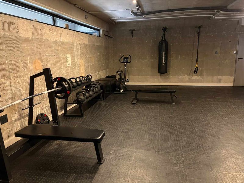 A functional home gym space featuring exposed concrete walls, industrial-style ceiling piping, and durable rubber flooring.