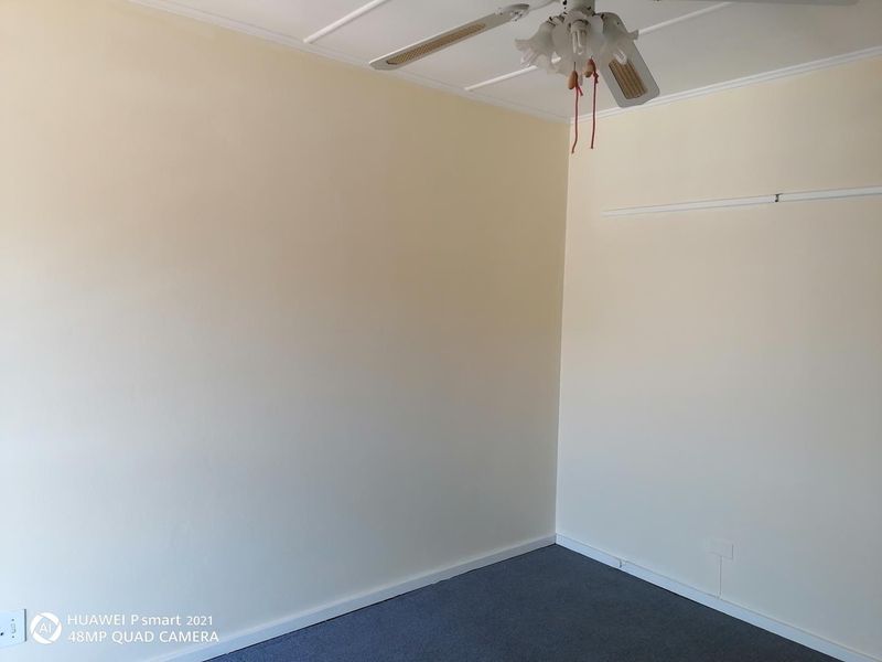 An empty bedroom featuring neutral walls, carpeted flooring, and a ceiling fan, providing a blank canvas for personalization.