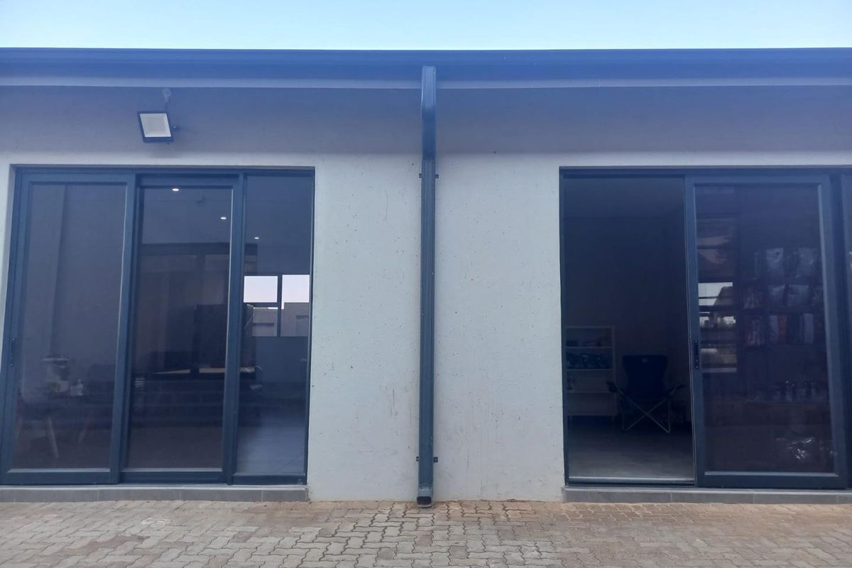 Rear exterior view of the apartment featuring dual sliding glass doors, a paved patio area, and functional exterior lighting.