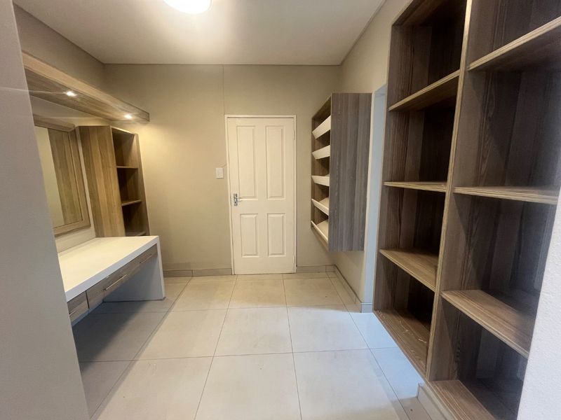 A spacious dressing room or bedroom area featuring extensive built-in cabinetry, a dedicated vanity station, and neutral tiled flooring.