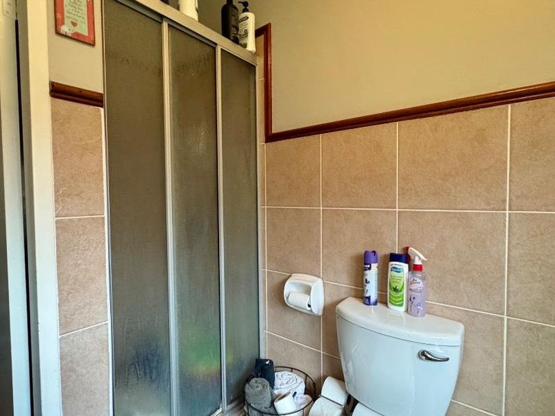 A functional bathroom featuring a shower enclosure, toilet, and neutral ceramic wall and floor tiling.