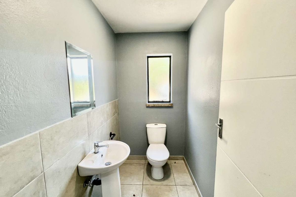 A compact guest bathroom featuring a pedestal sink, a wall-mounted mirror, and a standard toilet with tiled flooring and partial wall tiling.